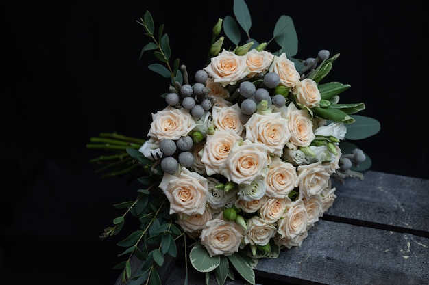 Beautiful wedding bouquet of bushy cream rose, eucalyptus, Brunei, Pittosporum and Lisianthus on a black wall. 