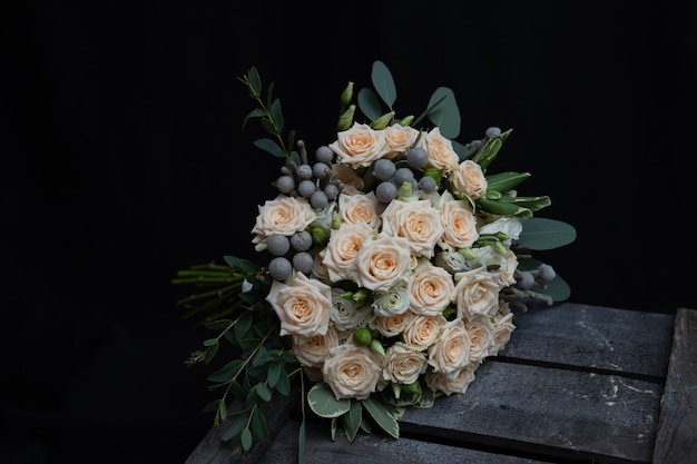 Beautiful wedding bouquet of bushy cream rose, eucalyptus, Brunei, Pittosporum and Lisianthus on a black wall. 