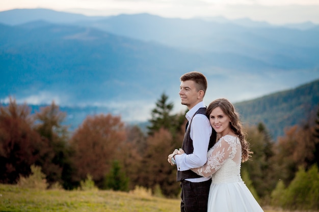 Beautiful wedding couple, bride and groom, in love on the wall of mountains. The groom in a beautiful suit and the bride in a white luxury dress. Wedding couple is walking