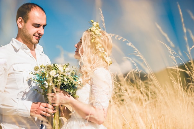 Beautiful wedding couple walking on field, bride and groom posing on wheat field with blue sky.