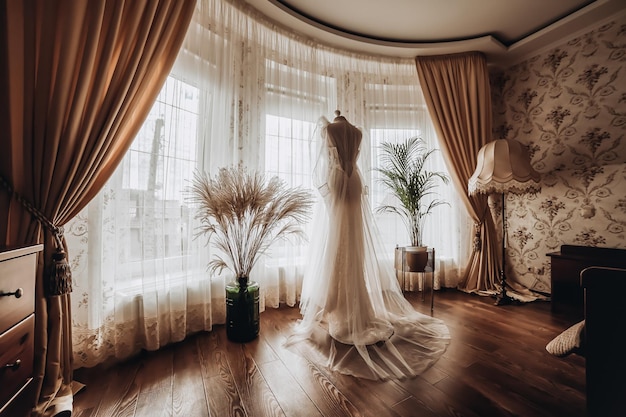 Beautiful wedding dress hanging in the room woman getting ready before ceremony