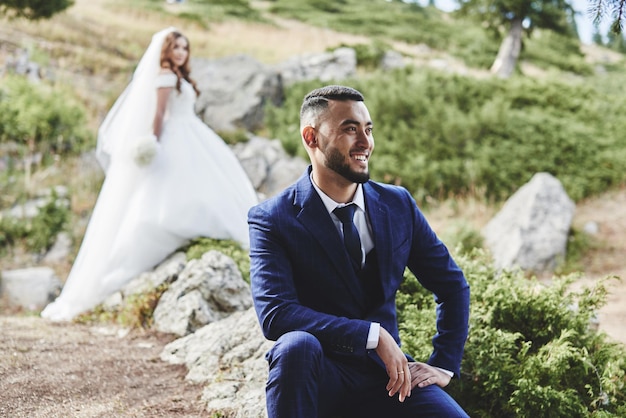 Photo beautiful wedding photo on mountain lake. happy asian couple in love, bride in white dress and groom in suit are photographed against background of the kazakh landscape