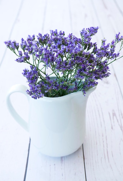 Beautiful white jug with purple kermek flowers on a light wooden background