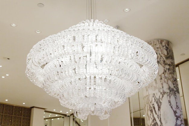 A beautiful white large crystal chandelier hangs on the ceiling in a bright room