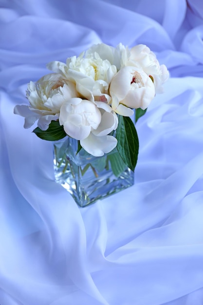 Beautiful white peonies in vase on fabric background