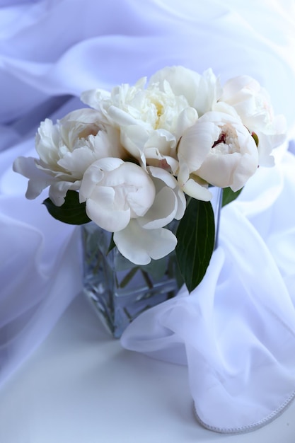 Beautiful white peonies in vase on fabric background