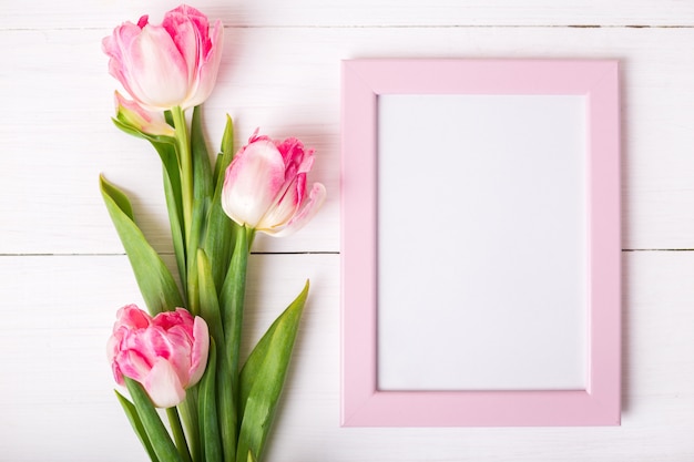 Beautiful white and pink tulips and photo frame for your text on white wooden background.