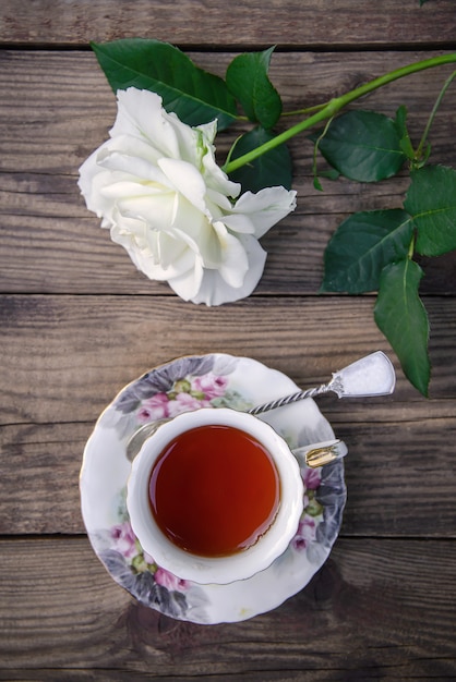 A beautiful white rose and a cup of tea on a rustic wooden background