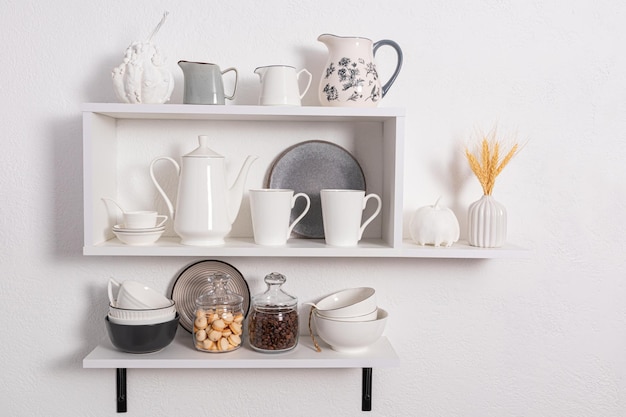 Beautiful white shelves with kitchen utensils on a white textured wall kitchen interior in white tones front view ecologically clean kitchen