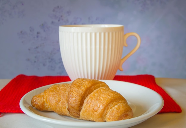 Beautiful white tea Cup with a croissant on red knitted scarf