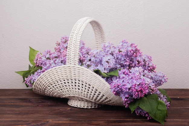 Beautiful white vintage wicker basket on a wooden table Lilac flowers in a retro basket