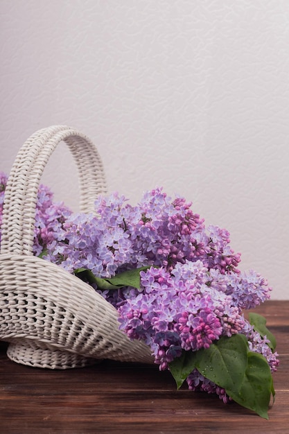 Beautiful white vintage wicker basket on a wooden table Lilac flowers in a retro basket