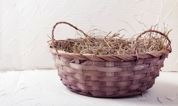 Beautiful wicker basket with hay on a white textured background.