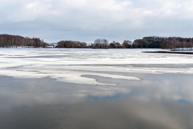 Photo beautiful winter landscape forest on the lake shore on a sunny frosty day panorama of the coastline covered with snow and birch grove ice on the river and the reflection of clouds in the water