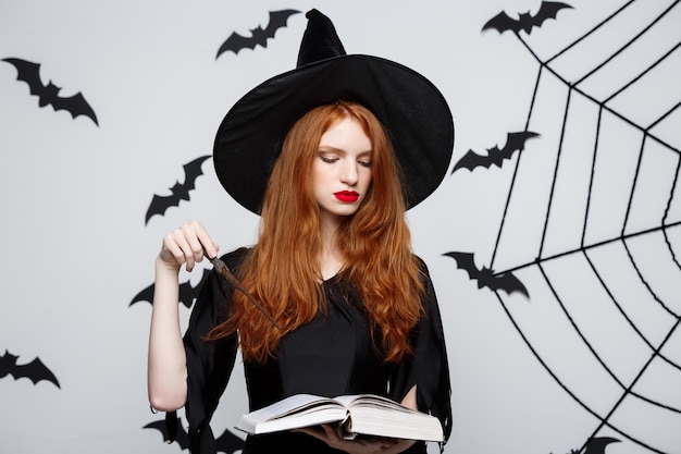 Beautiful Witch playing with magic stick on grey background.