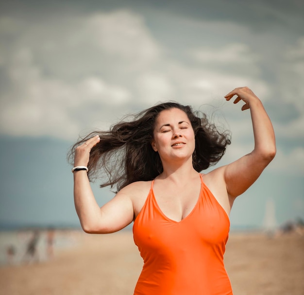 Beautiful woman 40 years old plus size, on the beach in an orange swimsuit, body positivity theme