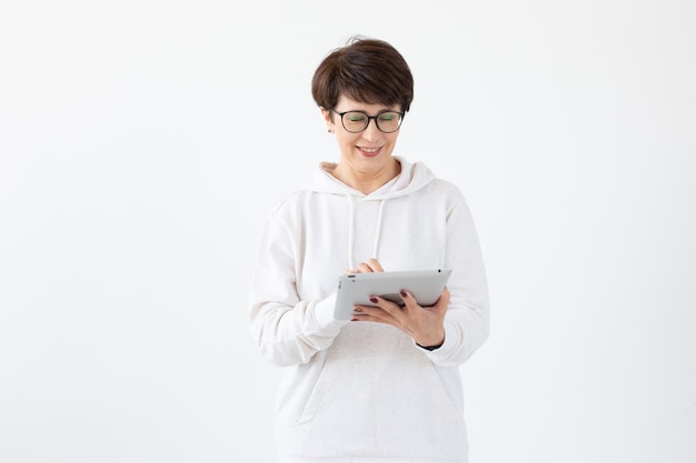 Beautiful woman 50 years old with short hair holding tablet on white wall with copy space