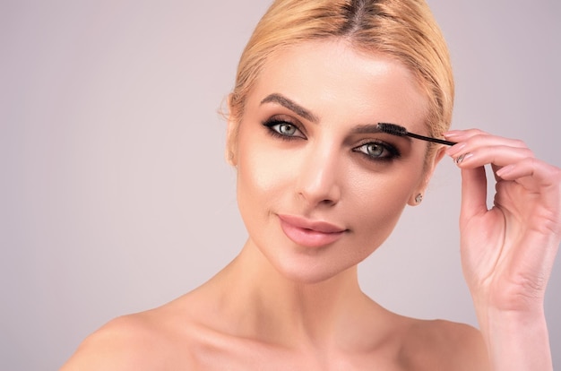 Photo beautiful woman applies brow gel with brows brush to her eyebrow studio portrait of young woman