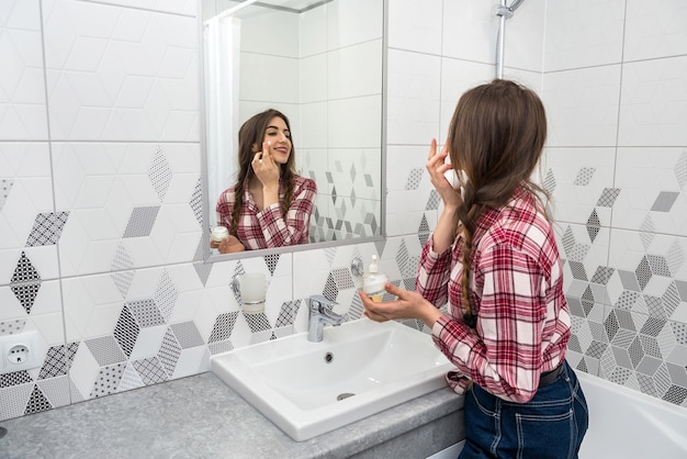 Beautiful woman applying cleansing moisturizing skin cream on face after bath. Skincare