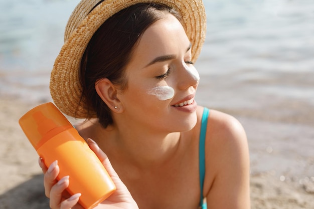 Photo beautiful woman applying cream sunscreen on tanned face sun cream skin and body care