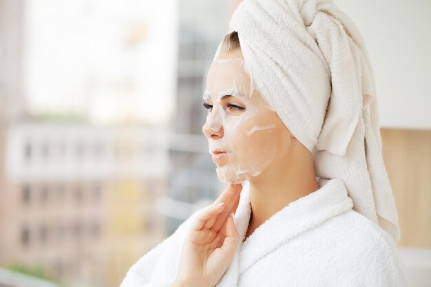 Beautiful woman applying paper sheet mask on her face white