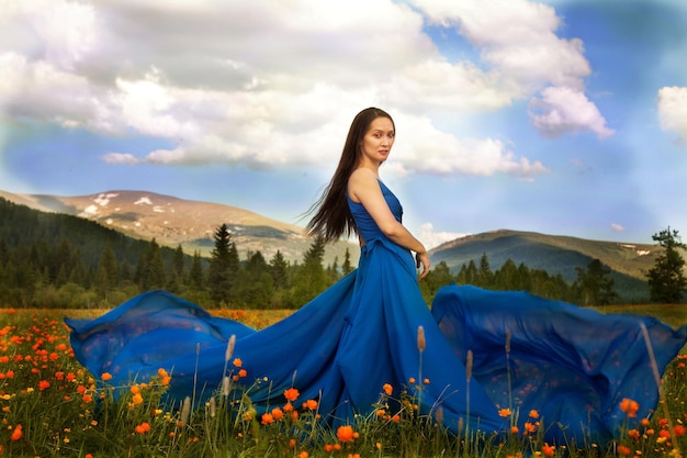 A beautiful woman of Asian appearance in a blue dress walks in a green meadow with orange flowers in the Altai mountains in summer. concept beauty, tourism.