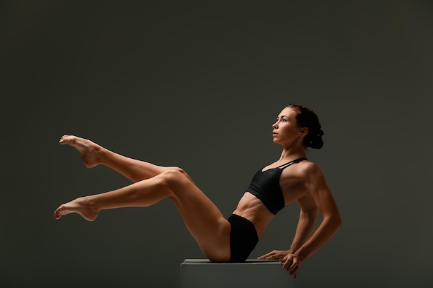 Beautiful woman ballet dancer in black swimsuit posing on light grey studio background Animal instinct