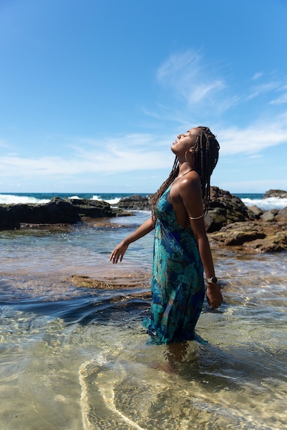 Beautiful woman in blue clothes and braided hair standing in the water on the beach walking and posing for a photo