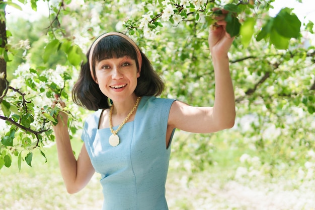 A beautiful woman in a blue dress under a flowering tree in the garden in spring. The brunette smiles and is happy