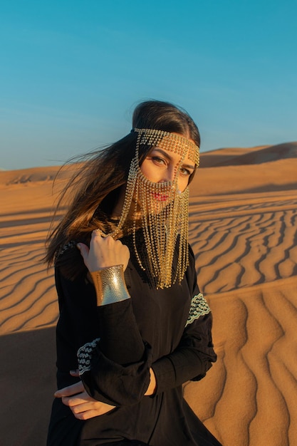 Beautiful woman in brilliant Burqa mask among the Dubai desert at sunset timeArabian style