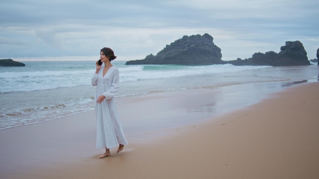 Beautiful woman calling smartphone at ocean beach relaxed lady walk sandy coast