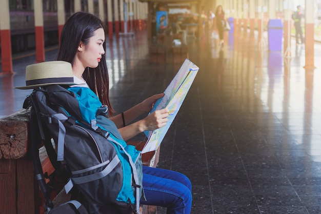 Beautiful woman carrying a backpack carrying a map of a railway station.