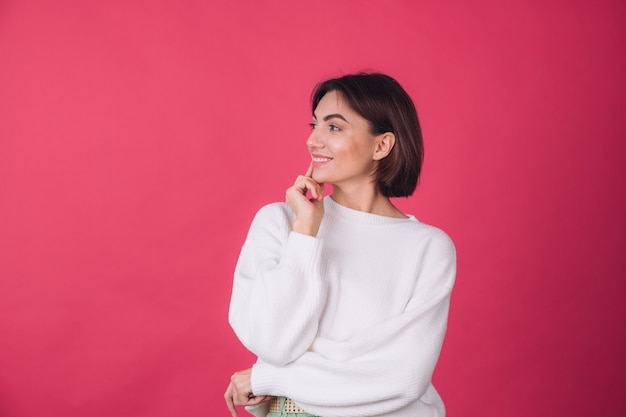 Beautiful woman in casual white sweater on red wall