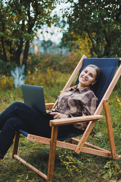 Beautiful woman in checkered shirt with laptop working outdoors in garden home office concept Remote work