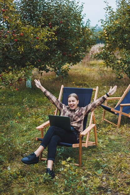 Beautiful woman in checkered shirt with laptop working outdoors in garden home office concept Remote work