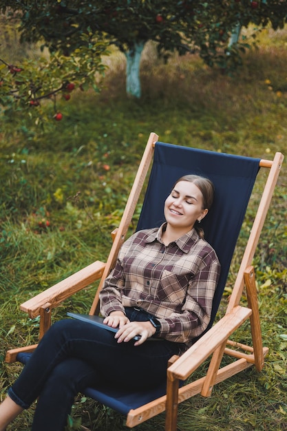 Beautiful woman in checkered shirt with laptop working outdoors in garden home office concept Remote work