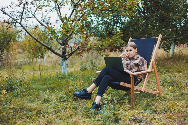 Beautiful woman in checkered shirt with laptop working outdoors in garden home office concept Remote work