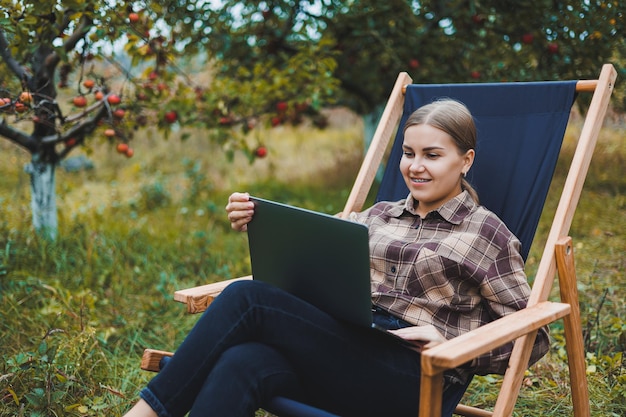 Beautiful woman in checkered shirt with laptop working outdoors in garden home office concept Remote work