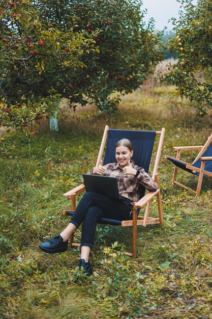 Beautiful woman in checkered shirt with laptop working outdoors in garden home office concept Remote work