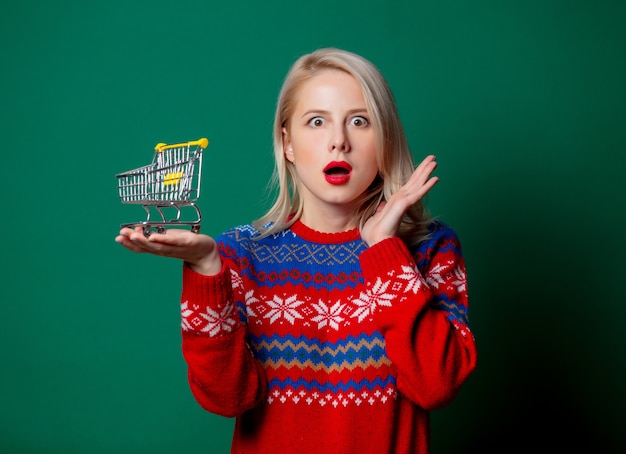 Beautiful woman in Christmas sweater holds shopping cart  