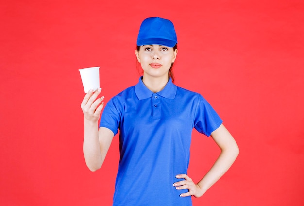 Beautiful woman courier in blue outfit posing with cup of tea on red.