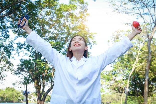 The beautiful woman doctor stretched out both arms in her hand, holding a red heart and Stethoscope