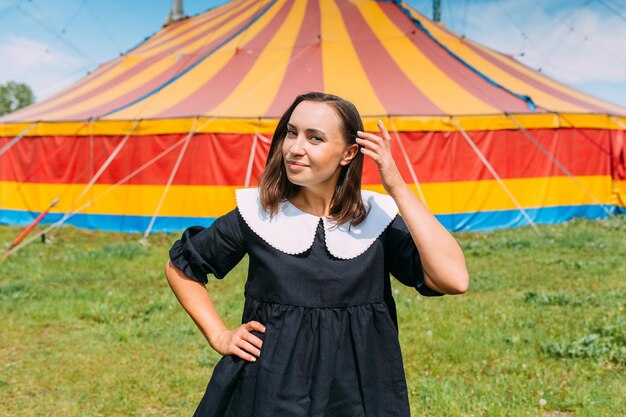 Beautiful woman in dress poses against backdrop of circus tent on sunny day