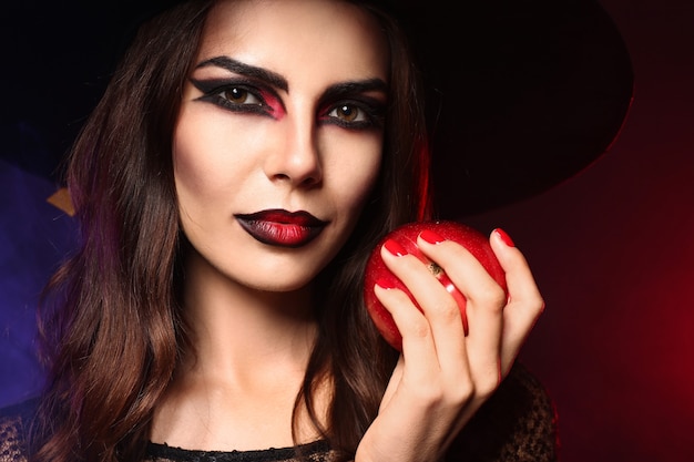 Beautiful woman dressed as witch for Halloween with apple on dark color