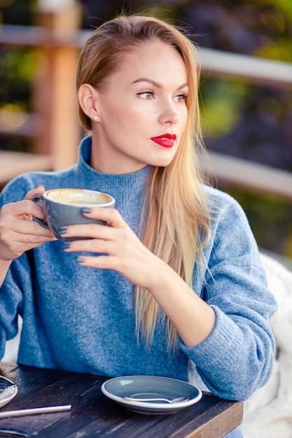 beautiful woman drinking coffee in autumn park under fall foliage