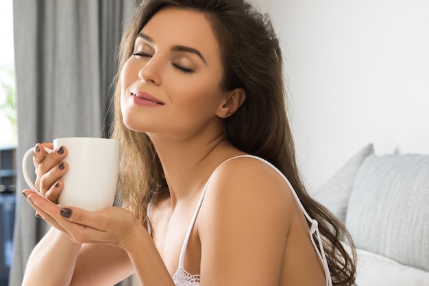 Beautiful woman drinking coffee or tea in bedroom