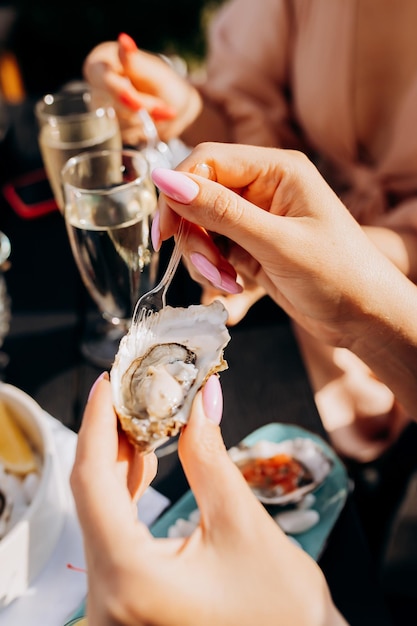 Beautiful Woman eating fresh oysters and drinking chilled prosecco wine on the summer sunset in restaurant Seafood delicacies