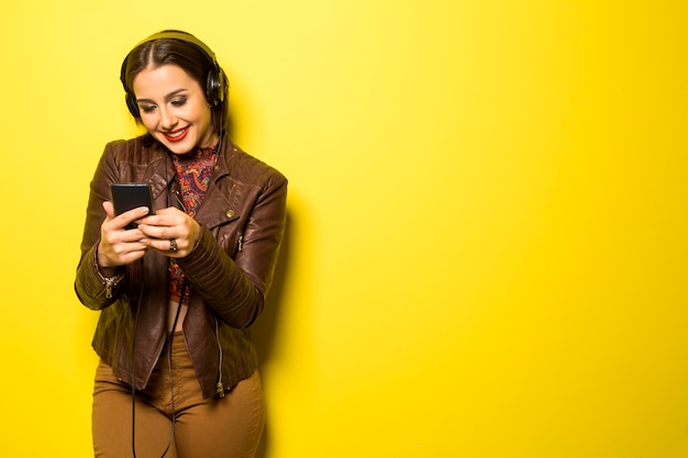 Beautiful woman enjoying music with the head phones in yellow wall