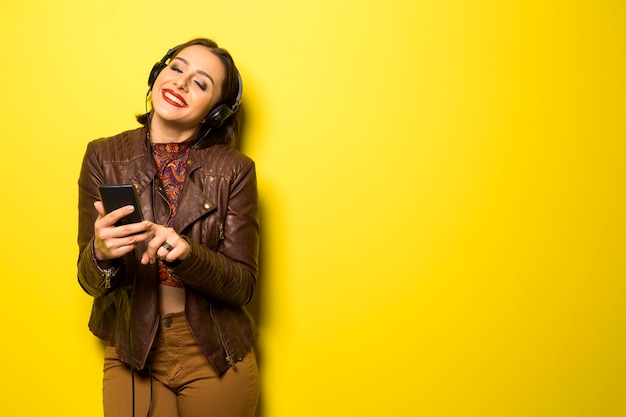 Beautiful woman enjoying music with the head phones in yellow wall