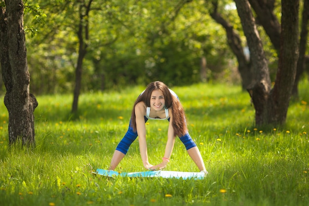 Beautiful woman exercising outdoors. Cheerful slim girl doing workout at the park in summer time